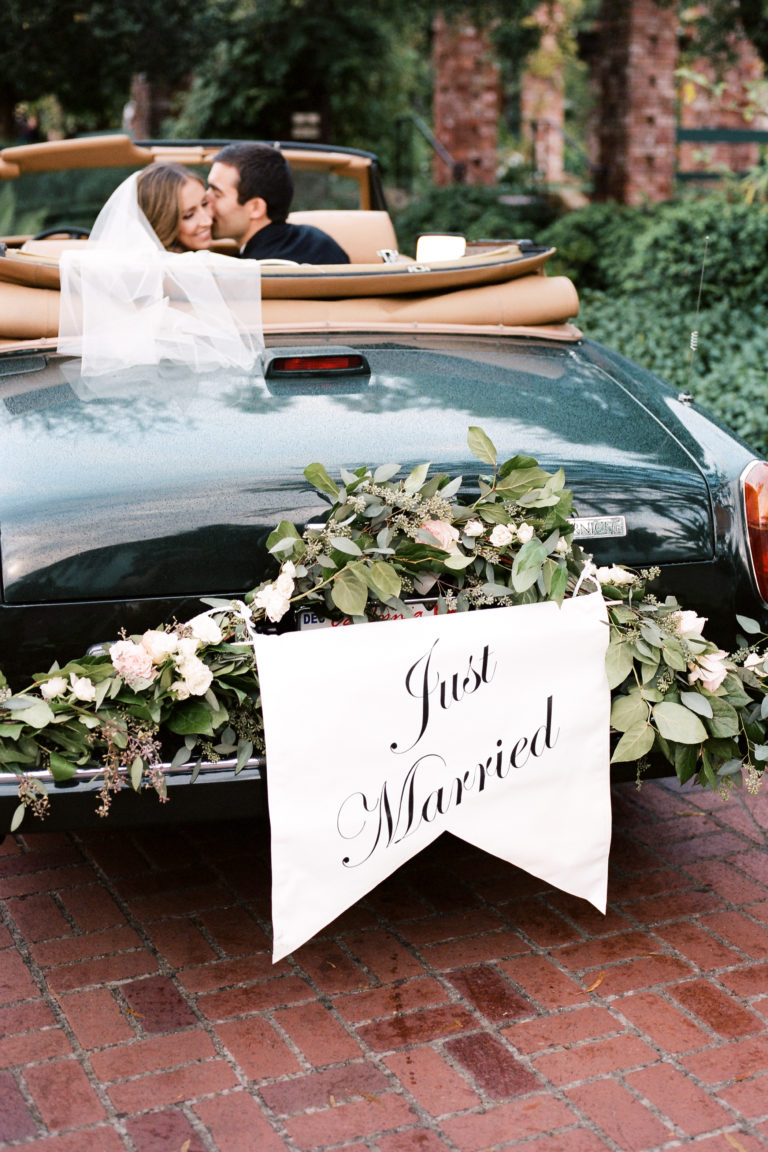 bride and groom in vintage car with just married sign