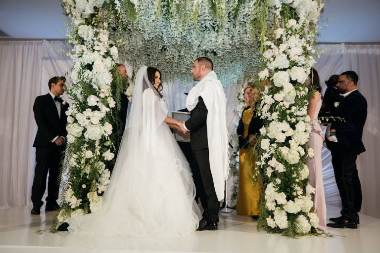 bride and groom under floral chuppah